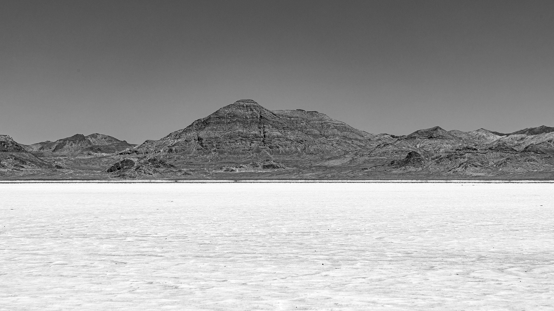 A flat plain of white salt stretches to a range of bare mountains under a clear sky.